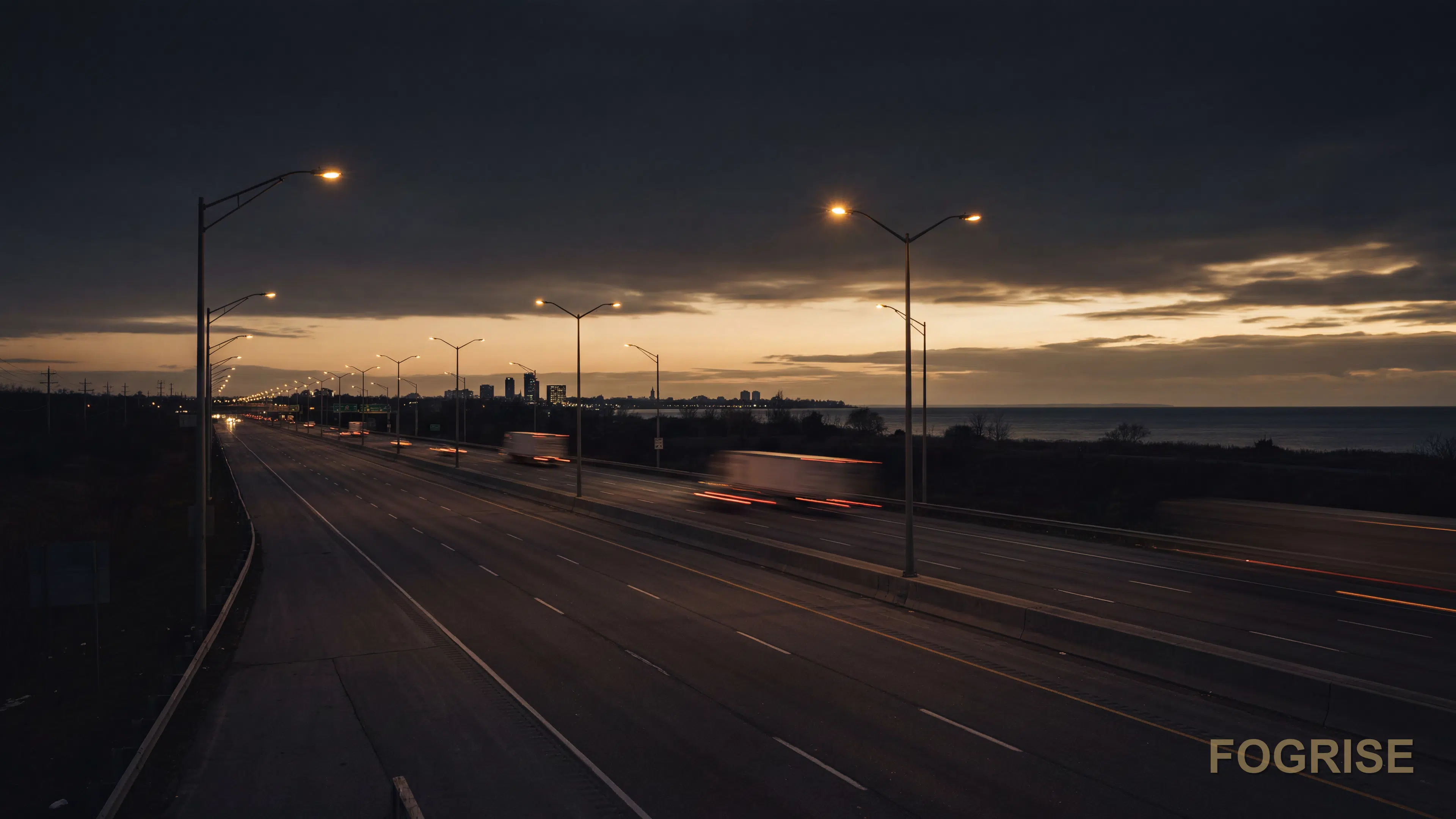 Dusk view of the Highway 401 corridor near Oshawa with the Durham Region skyline and Lake Ontario on the horizon in a dark editorial tone