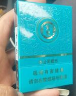 Jinsheng Qingci Mid cigarette packaging, close-up of the turquoise pack held in one hand