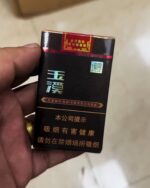 Yuxi Jingjie Mid cigarette packaging, front of the black and gold pack held in one hand