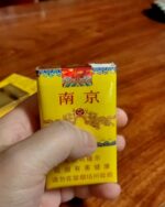 Nanjing Soft 95 Slim cigarette packaging, front of the yellow pack held over a wooden table